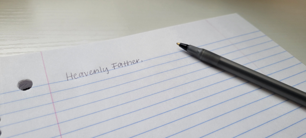 Hand writing “Heavenly Father,” to begin a handwritten prayer